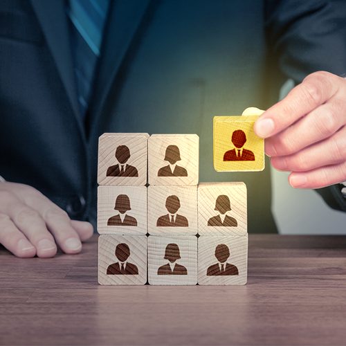 Imagem mostra um homem de terno encaixando peças que representam pessoas e uma delas em destaque de amarelo para mostrar o profissional que se destaca no mercado de trabalho.
