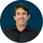 Imagem do CEO do Grupo Portfolio, Cassio Germano, em um fundo azul escuro. Ele é branco, tem cabelos lisos, está sorrindo e de blusa preta